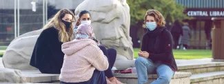 Image of 4 students wearing masks, sitting on the steps next to Queen's Tower