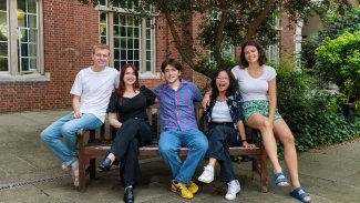 2024/25 Officer Trustees sitting on a bench outside in Beit Quad. They are smiling and seated together.